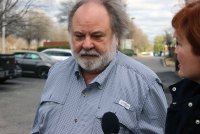 A photo shows a man walking outside as a reporter holds a microphone in front of him.