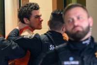 A photo of a man scowling at the camera as he is escorted indoors.